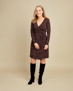 Woman wearing a patterned dress with long sleeves and knee-high boots on a beige background. This dress is the Appleton Wrap Dress sewing pattern from Cashmerette.