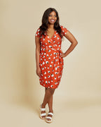 Woman wearing a red dress with white patterns on a beige background. This dress is the Appleton Wrap Dress sewing pattern from Cashmerette.