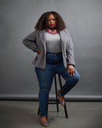 Woman sitting on a stool wearing a gray cardigan, white shirt, blue jeans, and gray shoes against a gray background. This blazer is the Auburn Blazer sewing pattern from Cashmerette.