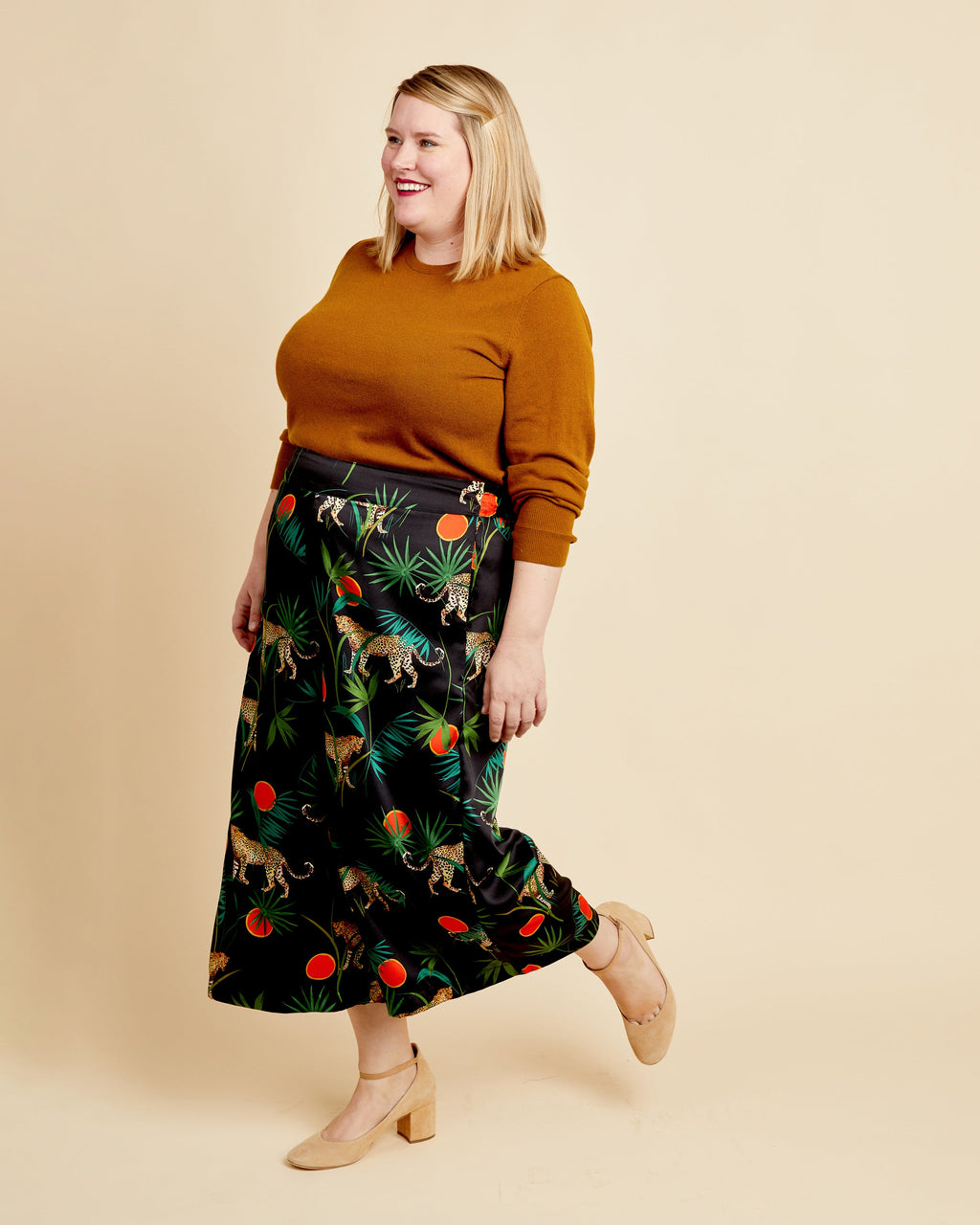 Woman wearing a mustard sweater and patterned skirt on a beige background. These pants are the Calder Pants & Shorts sewing pattern from Cashmerette.