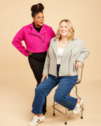 Two women posing together against a beige background. This biker jacket is the Canton Moto Jacket sewing pattern from Cashmerette.