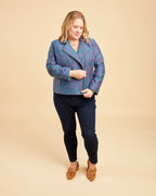 Woman wearing a blue patterned jacket and dark jeans on a beige background. This biker jacket is the Canton Moto Jacket sewing pattern from Cashmerette.