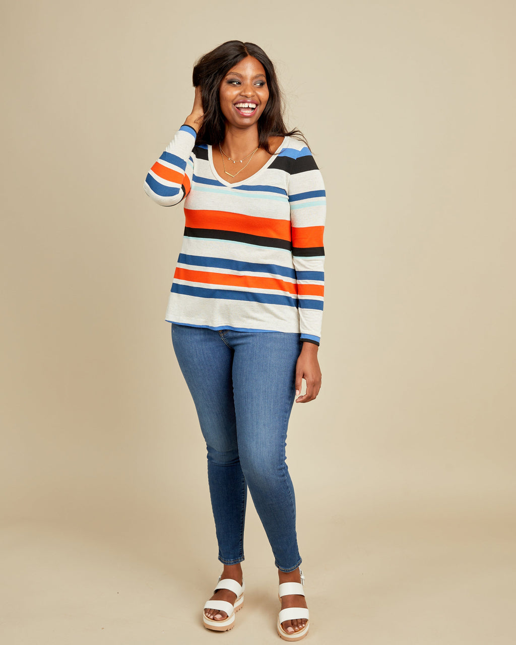 Woman wearing a striped sweater and blue jeans on a beige background. This t-shirt is the Concord T-Shirt sewing pattern from Cashmerette.