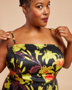 Woman wearing a black dress with colorful floral patterns on a beige background. This dress is the Ellington Strapless Dress sewing pattern from Cashmerette.