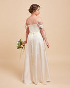 Woman in a white off-shoulder wedding dress holding a bouquet on a beige background. This dress is the Ellington Strapless Dress sewing pattern from Cashmerette.