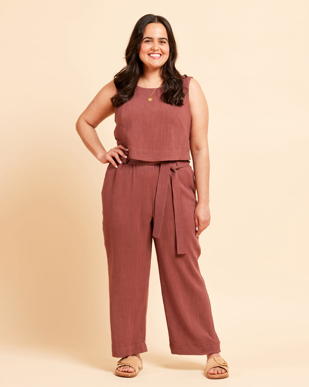 Woman wearing a brown top and brown pants in front of a yellow background. These shorts are the Everett Pants & Shorts sewing pattern from Cashmerette.