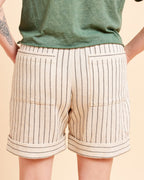 Beige shorts with black stripes worn by a person on a beige background. These shorts are the Everett Pants & Shorts sewing pattern from Cashmerette.