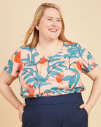 Woman wearing a colorful floral top and navy wide-leg pants on a beige background. This is the Montrose Top sewing pattern from Cashmerette.