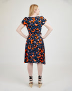 Woman wearing a patterned dress on a plain background. This dress is the Roseclair Wrap Dress sewing pattern from Cashmerette.
