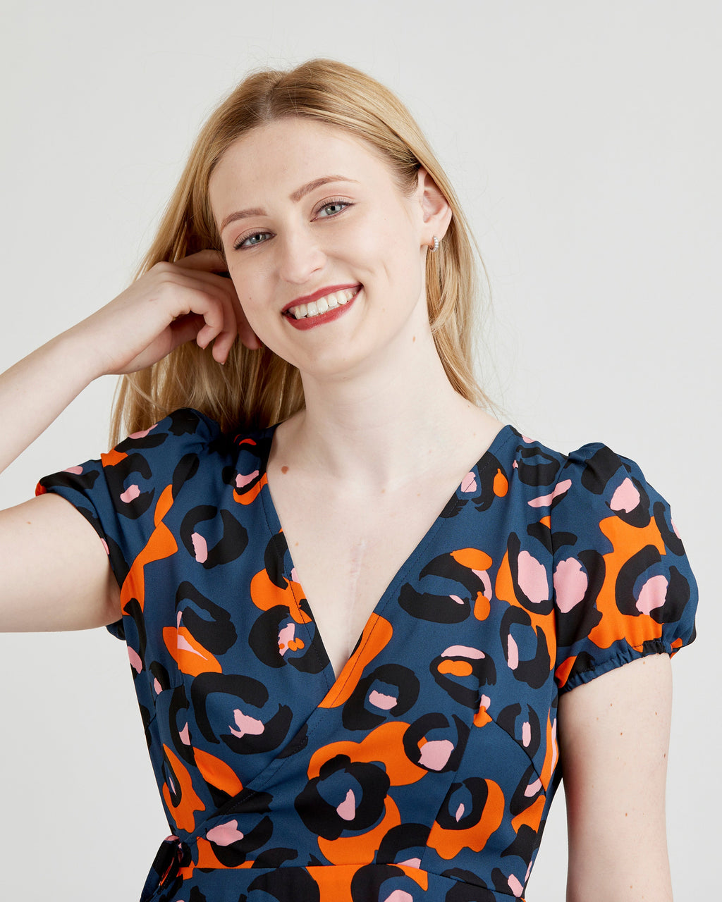 Woman wearing a blue dress with orange and pink abstract pattern on a plain background. This dress is the Roseclair Wrap Dress sewing pattern from Cashmerette.
