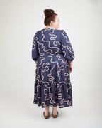 Woman wearing a navy dress with pink wavy patterns on a white background. This dress is the Roseclair Wrap Dress sewing pattern from Cashmerette.