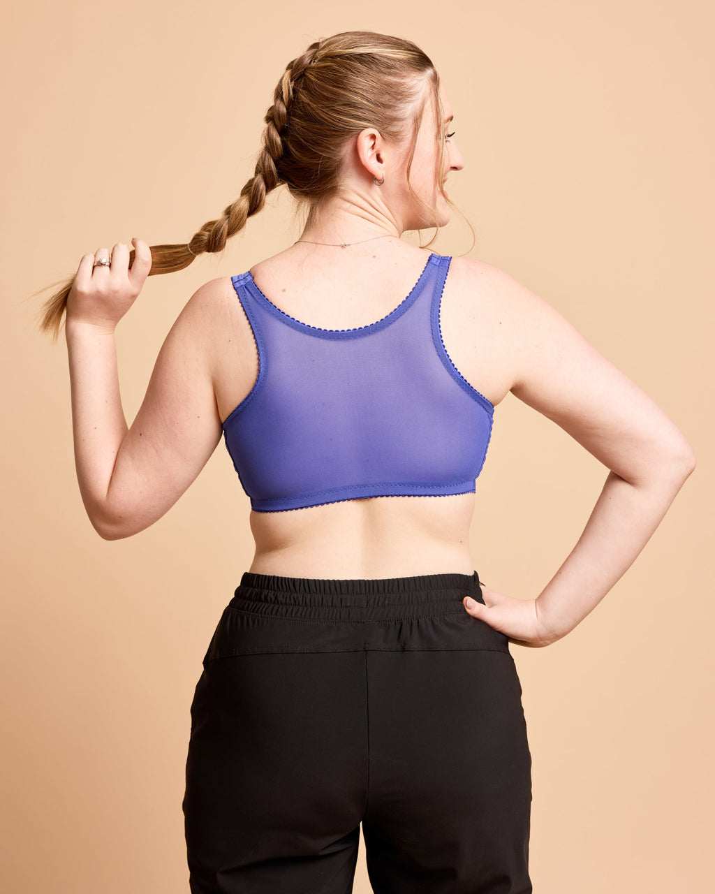Woman wearing a purple sports bra and black leggings against a beige background. This is the Cashmerette Somerville Sports Bra sewing pattern for big boobs.