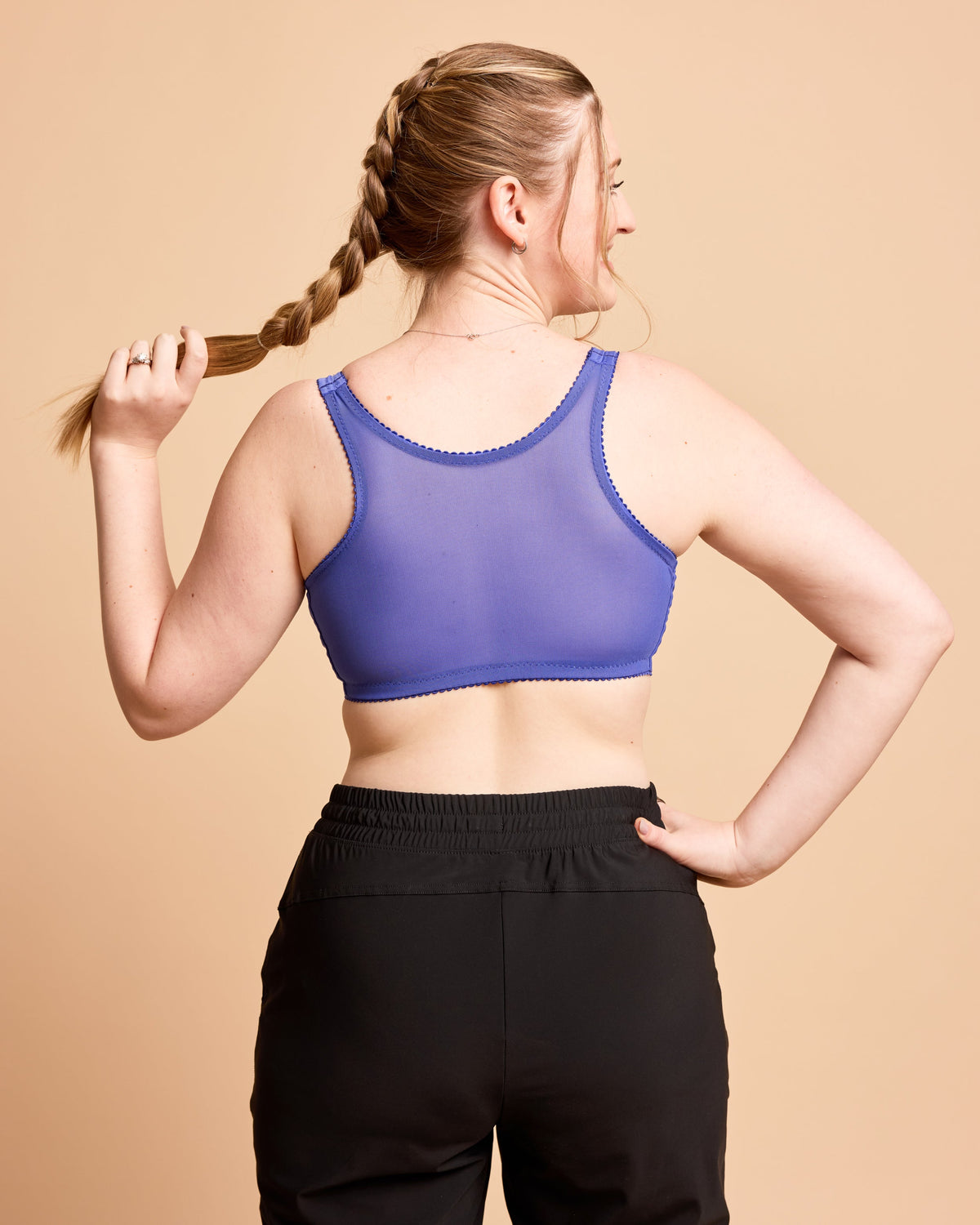 Woman wearing a purple sports bra and black leggings against a beige background. This is the Cashmerette Somerville Sports Bra sewing pattern for big boobs.