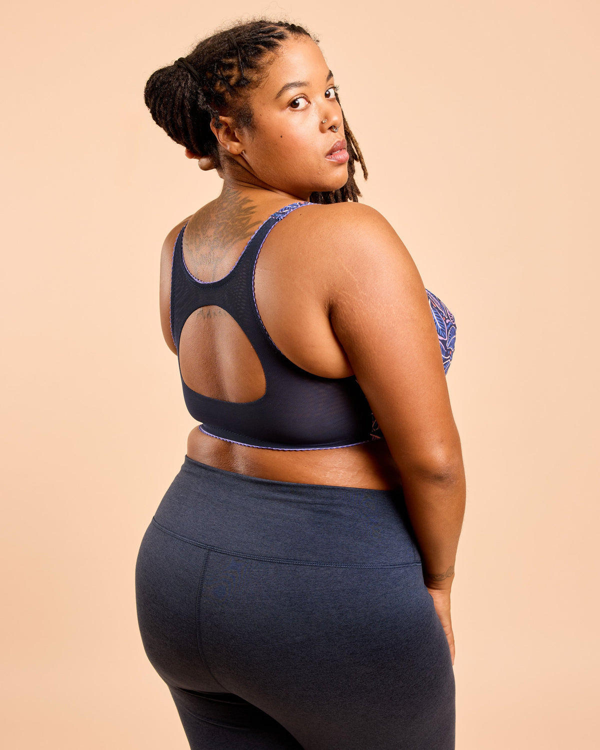 Woman wearing a black sports bra and leggings on a beige background. This is the Cashmerette Somerville Sports Bra sewing pattern for big boobs.