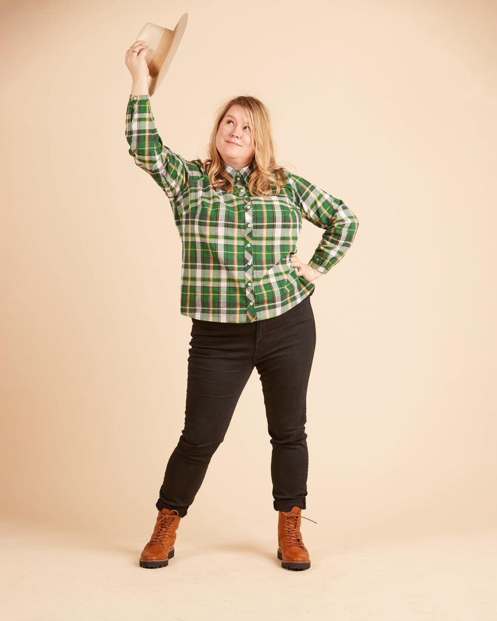 Person wearing a green plaid shirt, black pants, and brown boots against a beige background. This top is the Vernon Shirt sewing pattern from Cashmerette.
